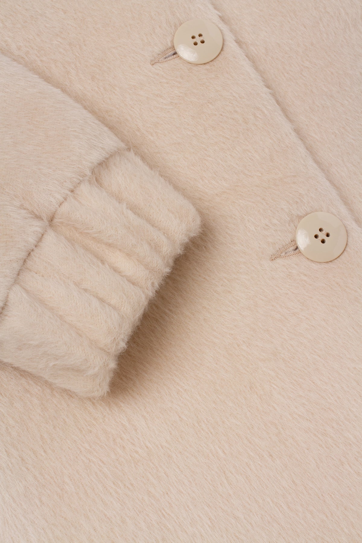 Close-up of a cream-colored fuzzy faux fur jacket with a ribbed cuff and cream buttons.