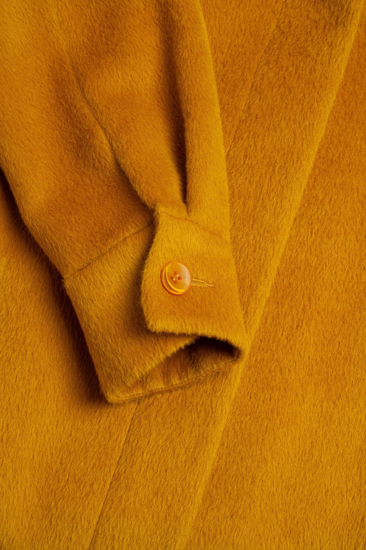Close-up of a mustard yellow coat with a button detail