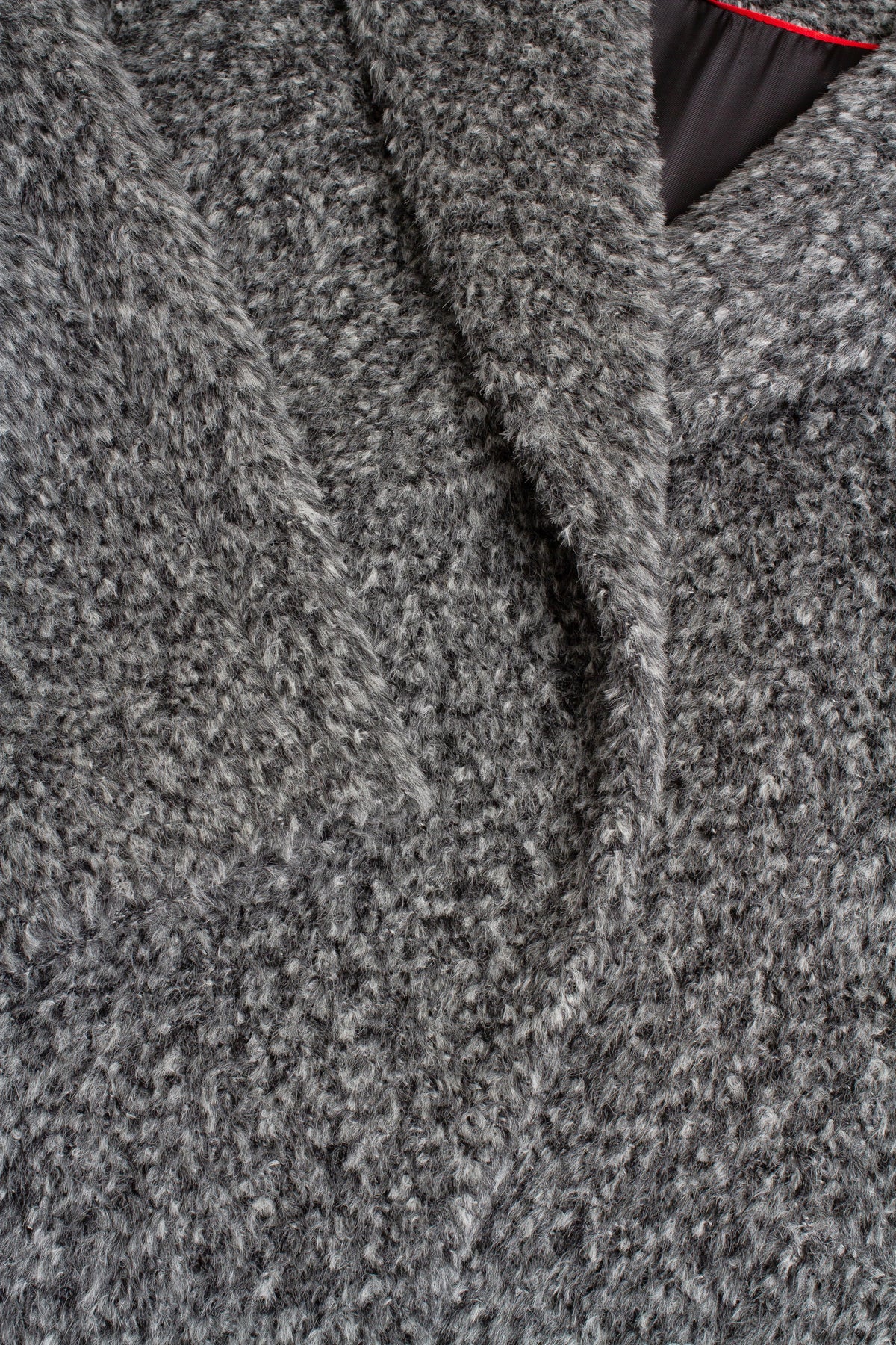 Close-up of a textured gray and white heathered fabric, showing the weave and a sliver of a black lining with a thin red edge.