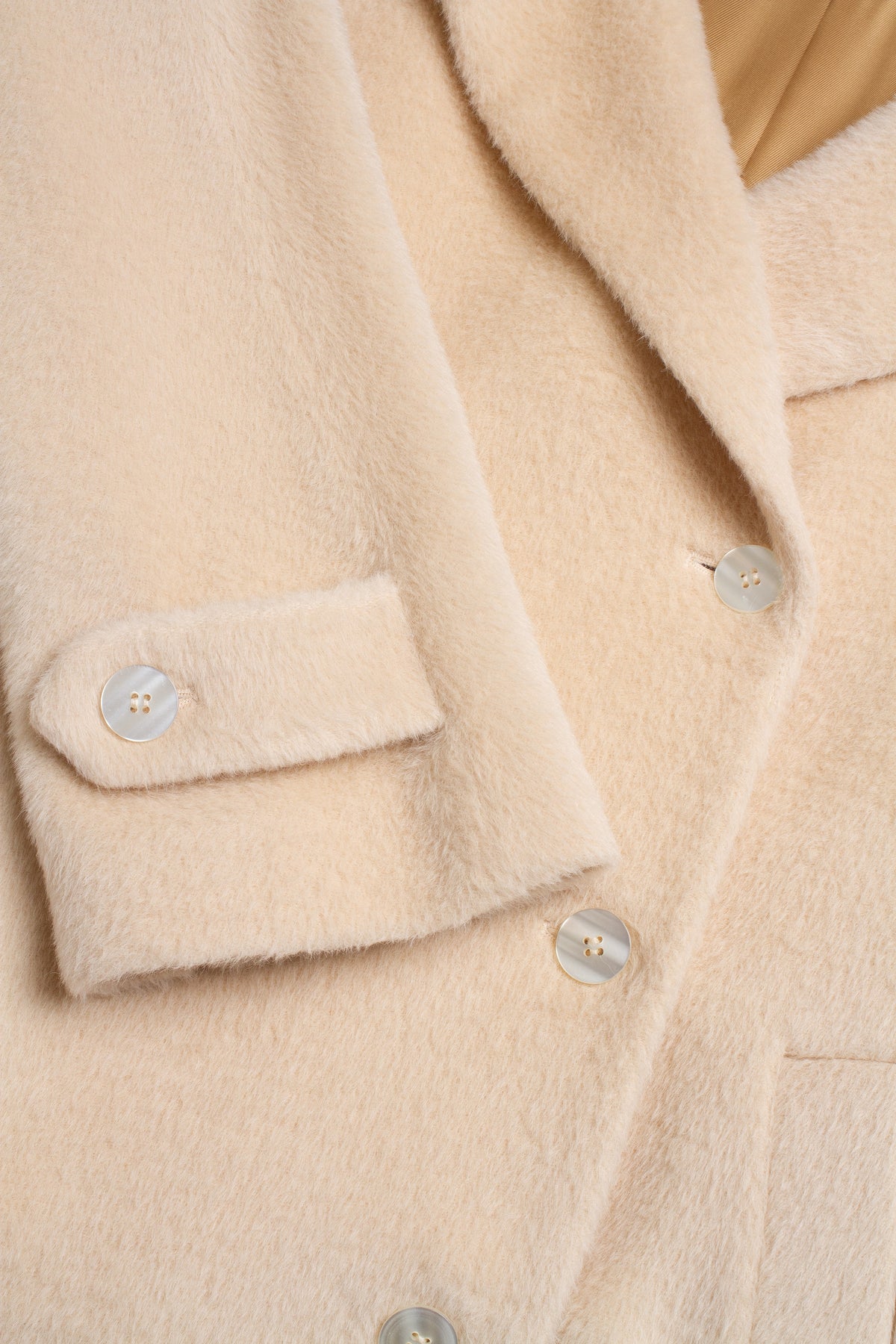 Close-up of a soft, fuzzy beige coat with a flap pocket and light-colored buttons.