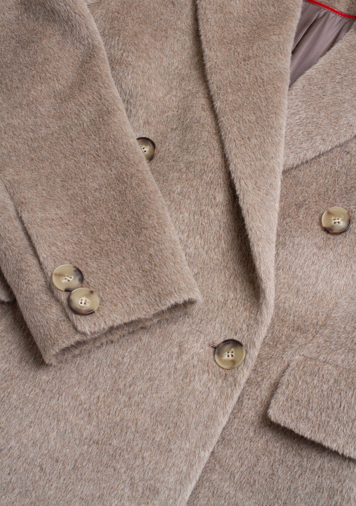 Close-up of a beige double-breasted coat with brown buttons, showing the soft textured fabric and lapels.